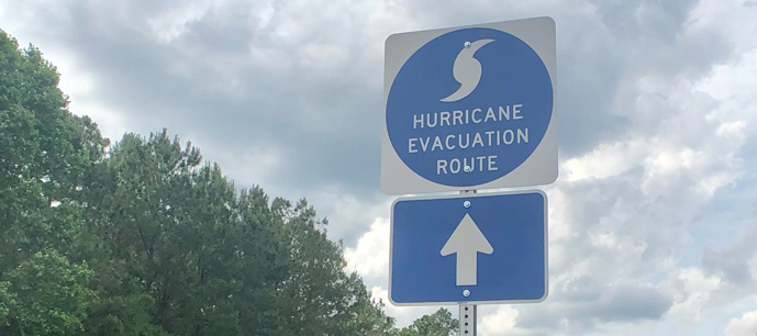 Hurricane Evacuation Route sign with arrow road sign on a background of trees and cloudy sky.