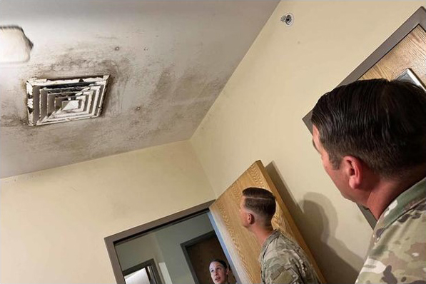 Photo of two men looking up at a ceiling vent with mold growth on the vent and ceiling.