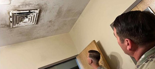 Photo of two men looking up at a ceiling vent with mold growth on the vent and ceiling.